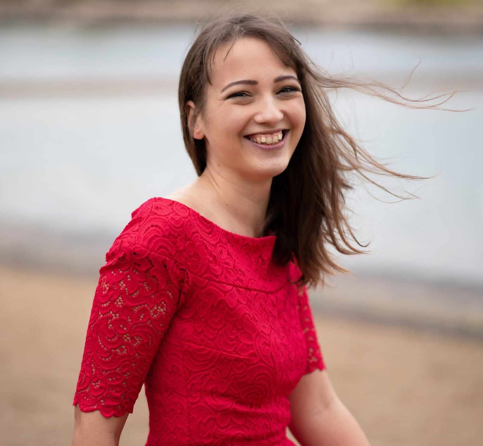 Autorin Jo Jonson, lachend im roten Kleid vor dem See der Leipziger Buchmesse