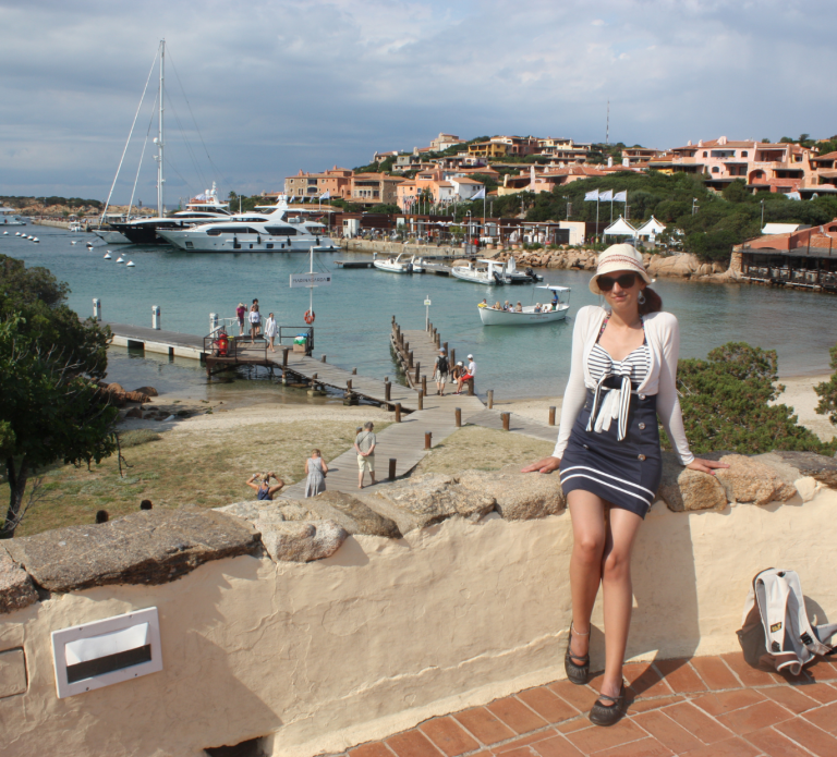 Jo Jonson sitzt auf Mauer vor tollem Hafen in Porto Cervo bei ihrem Urlaub auf Sardinien